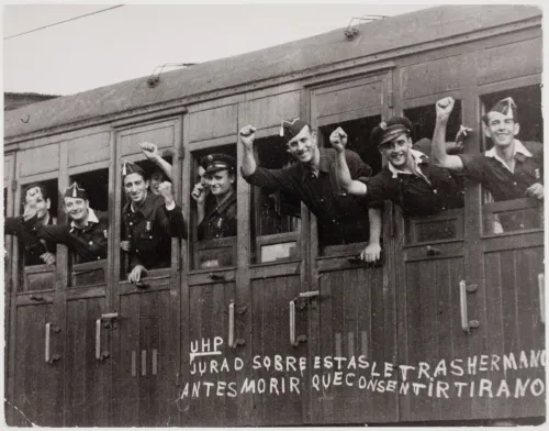 Young men in WWII waving their hands as they depart on a train.