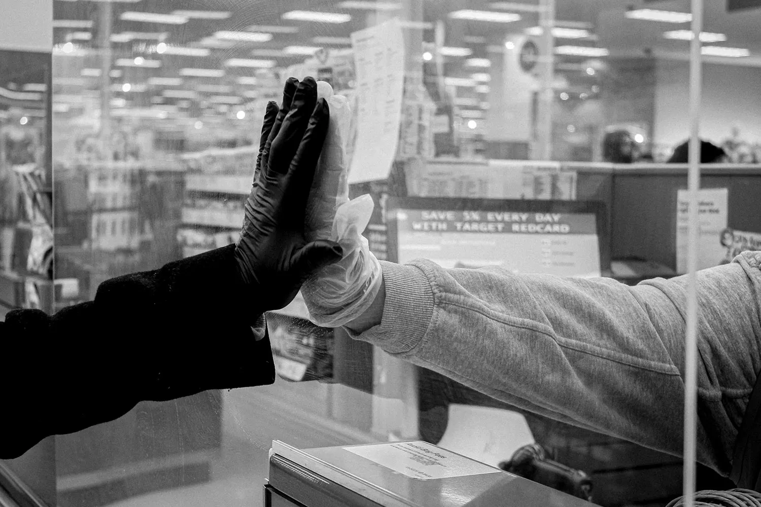 Two hands raised towards each other with a clear plastic barrier between them.