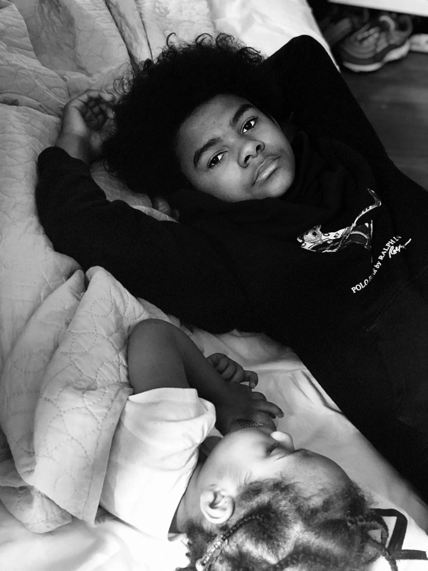 Two children laying in a bed, the younger sister is asleep while the older brother is looking at us.